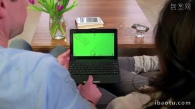 夫妇使用笔记本电脑与绿色屏幕的人和笔记本电脑显示器在家里的沙发